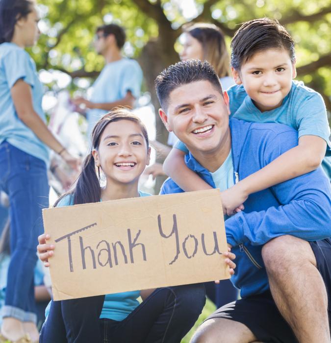 Family sitting close together holding up a thank you sign 